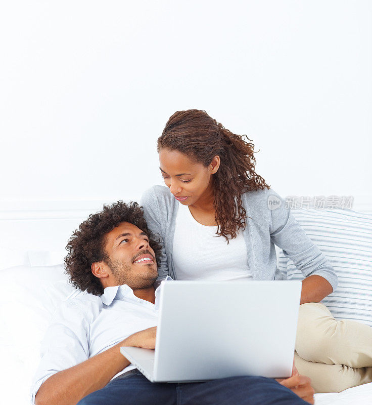 一个聪明快乐的年轻夫妇躺在床上，手提电脑的肖像
