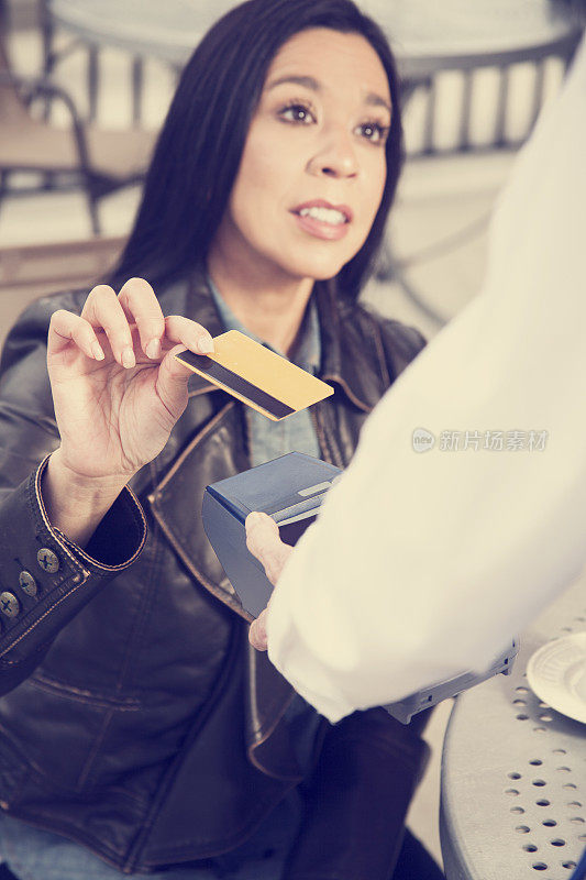 一位女士在户外咖啡馆用信用卡付咖啡钱。