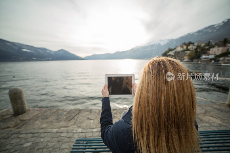 一名女子在湖边的长椅上用平板电脑拍照