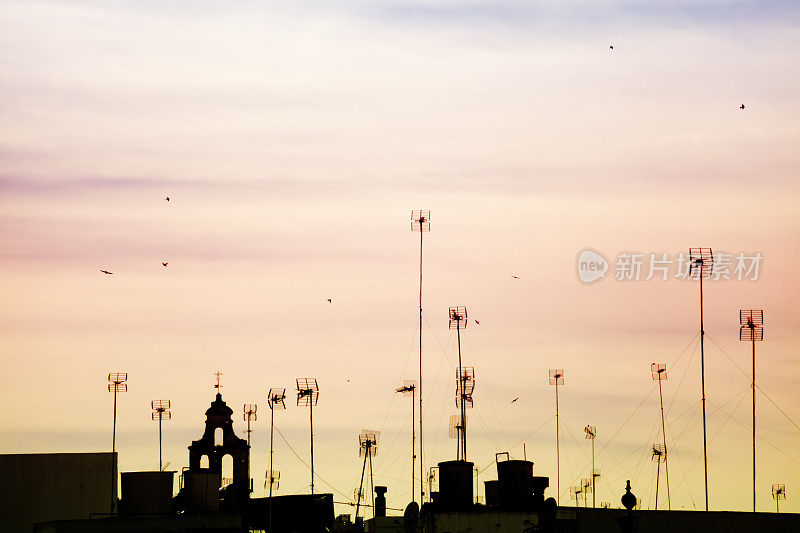 天线、烟囱和钟楼的剪影，夕阳的背景。