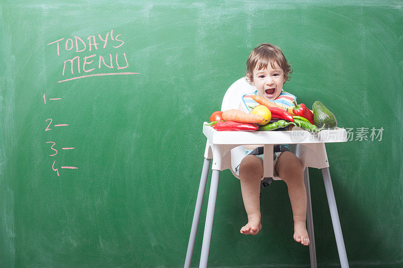 小男孩在绿色黑板前的高椅子上吃东西