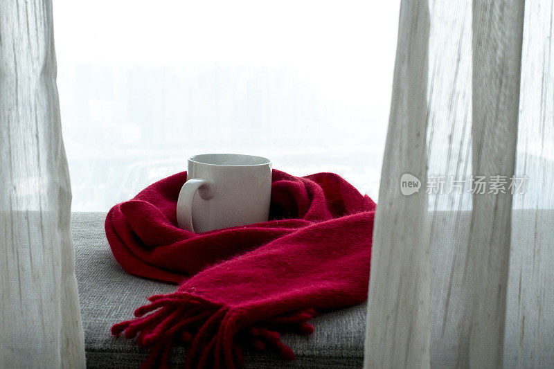 咖啡杯和红围巾放在窗边的沙发上