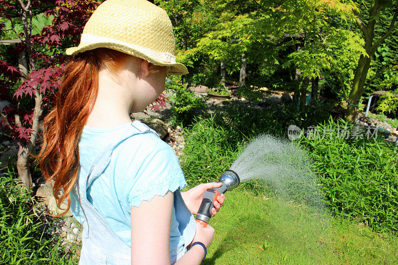 女孩用软管浇灌花园草坪的形象