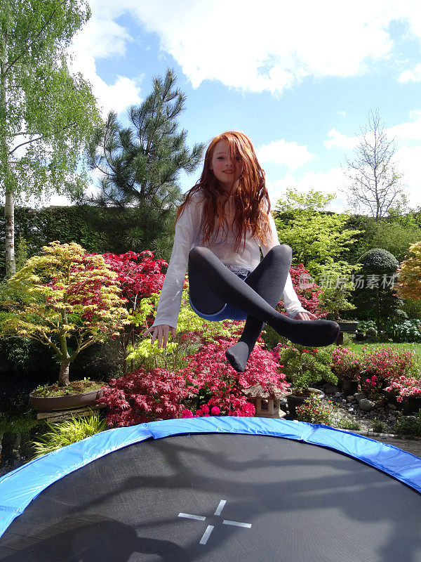 一个女孩坐在半空中，在花园里的蹦床上蹦跳