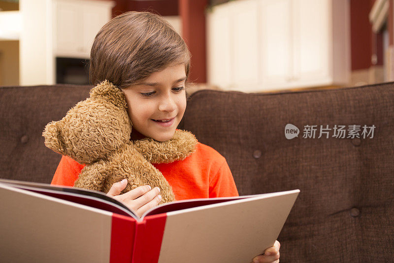 孩子在家里和泰迪熊一起看书。