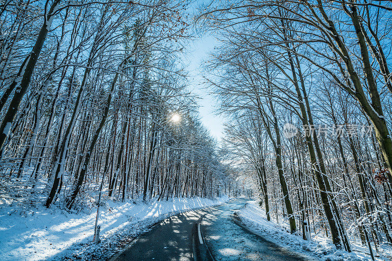 汽车旅行-在阳光明媚的冬日里，森林里霜冻的乡村道路