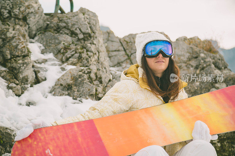 近景美丽的年轻女子在冬天的衣服站在一边，手拿木棍的背景雪山