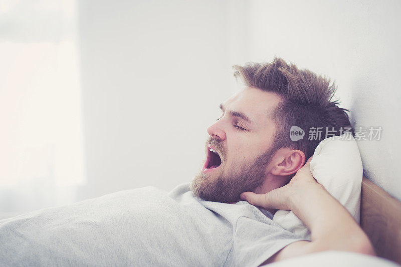 英俊年轻的美国男性在家里的床上打哈欠睡觉-保健概念。