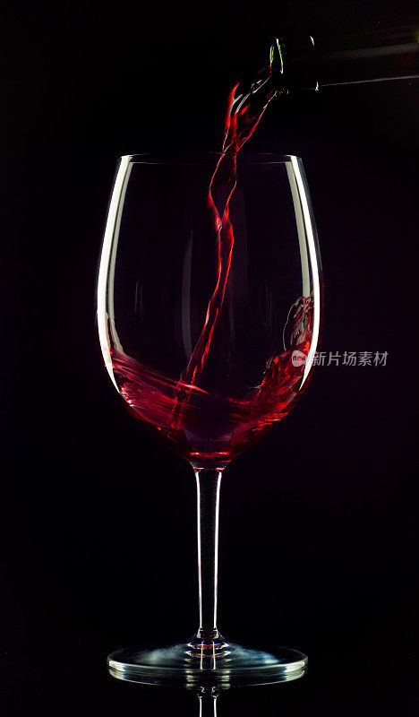 在黑色背景下，红酒被倒入玻璃杯中