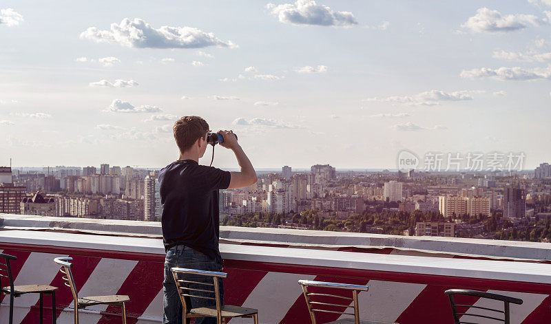 一个年轻人在屋顶上用双筒望远镜看东西