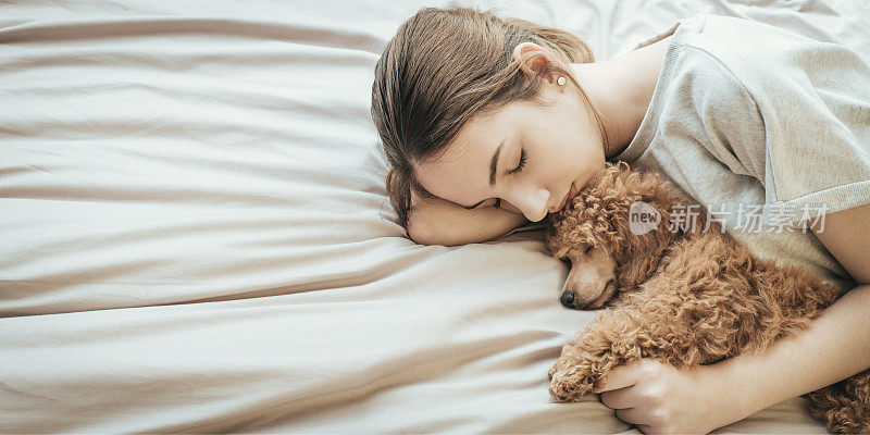 年轻女子躺在床上和狮子狗睡觉。