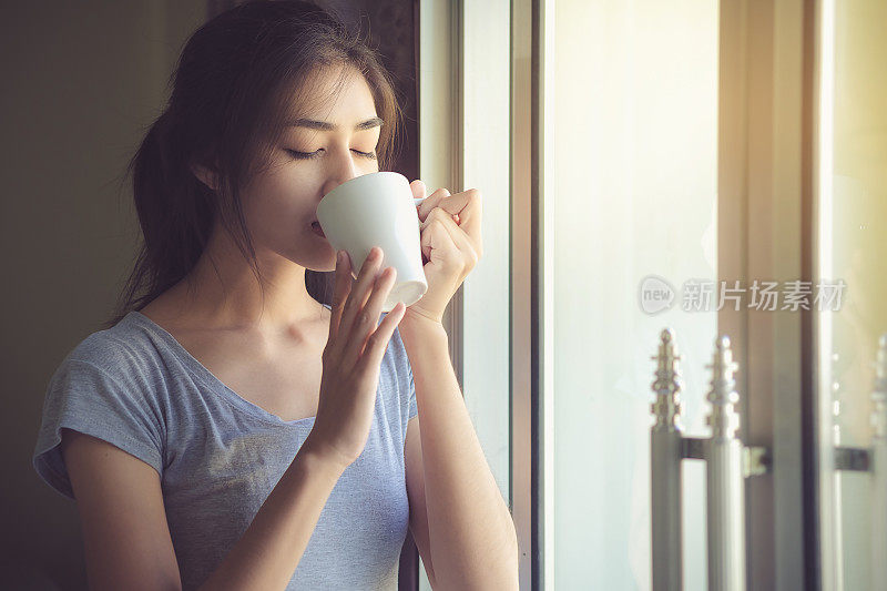 可爱的女人在周末愉快地喝着咖啡，窗外有一缕阳光。生活方式的概念