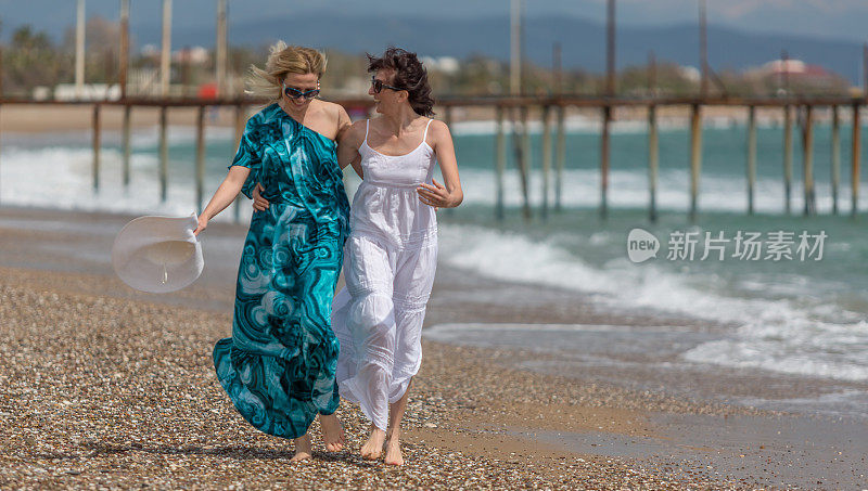 两个快乐的成熟女人微笑着走在沙滩上