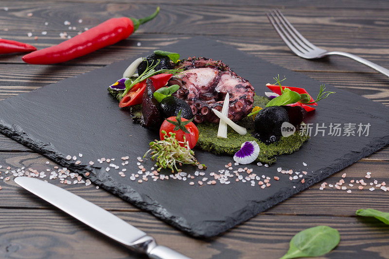烤章鱼配蔬菜在黑色页岩板上。美味的海鲜放在木板桌上的石板上。俯视图
