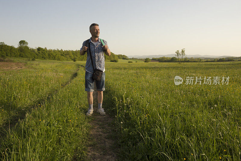 成年男子背着双肩包徒步穿越绿色草地