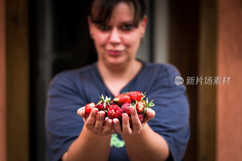 近距离的年轻女子抱着新鲜采摘的草莓在她的手中