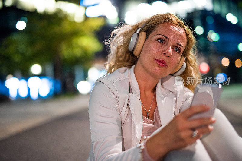 年轻的女商人在街上听着音乐。