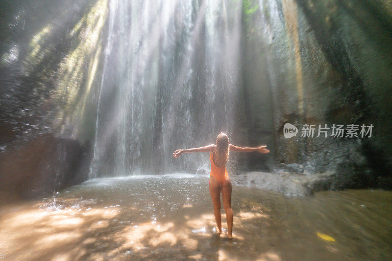 在巴厘岛的热带雨林中，旅行的年轻女子张开双臂拥抱大自然的美丽。人们以自然为旅游理念。