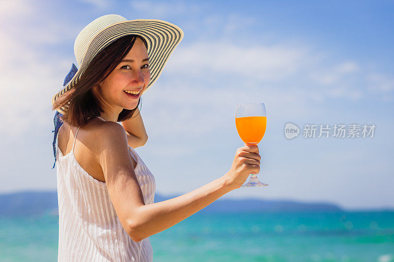 年轻快乐的亚洲女人与橙汁手在海滩上，度假和夏季概念，拷贝空间