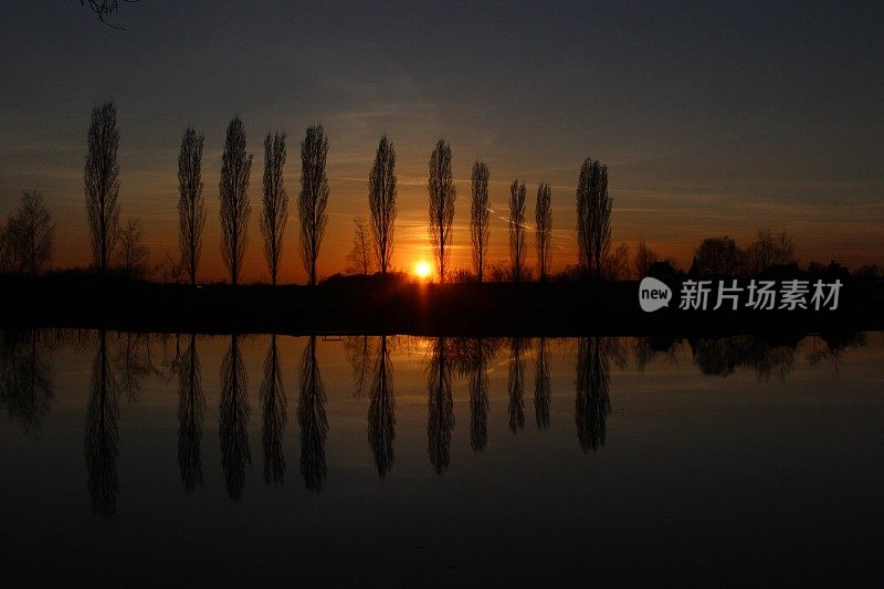 夕阳西下，树木倒映在湖面上