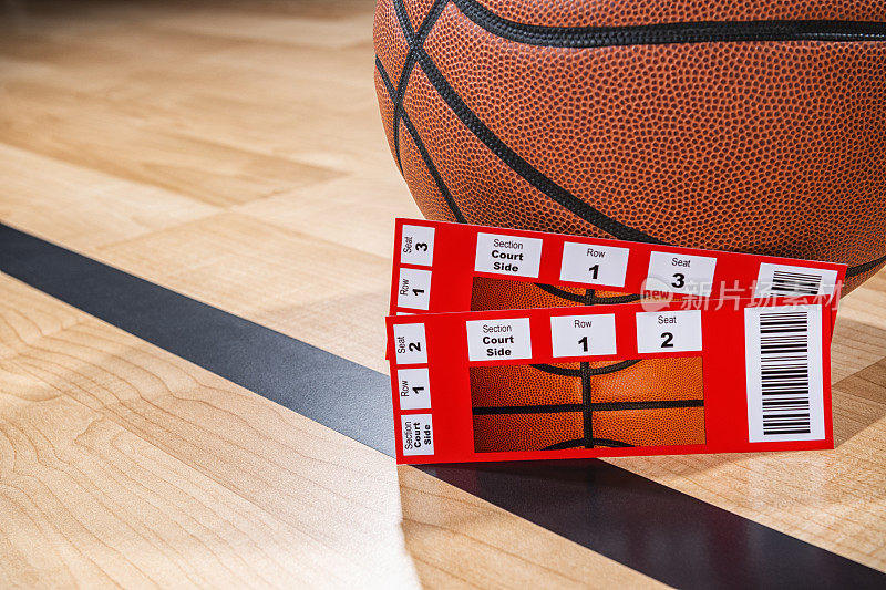 两张篮球票坐在一个球旁边，背景是竞技场的木地板