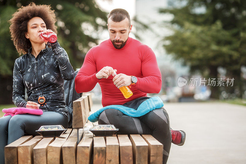 一对年轻的运动夫妇在城市公园运动后休息时给自己补水