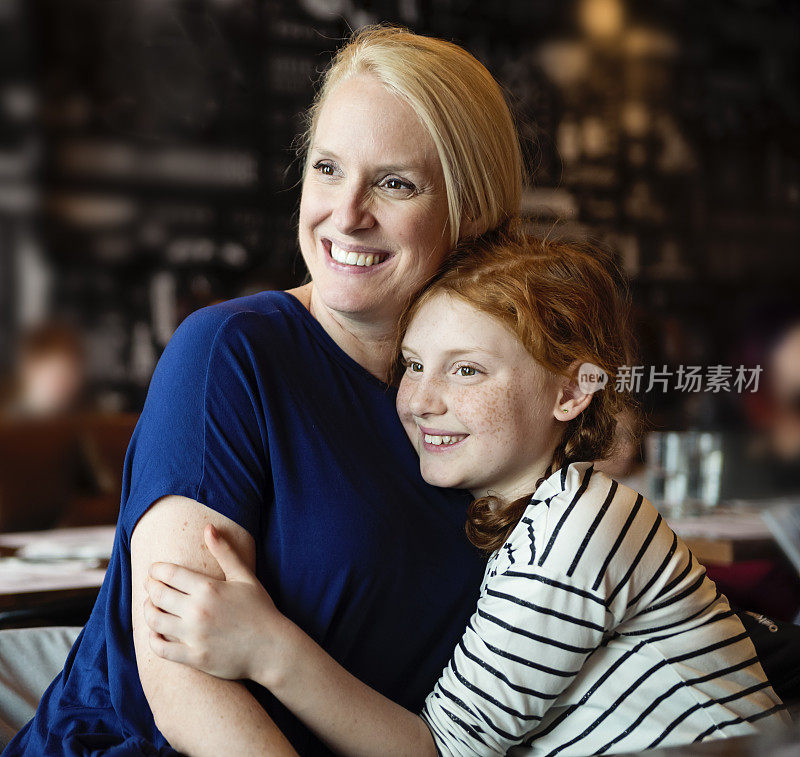 母亲和十来岁的女儿在餐桌前摆姿势。