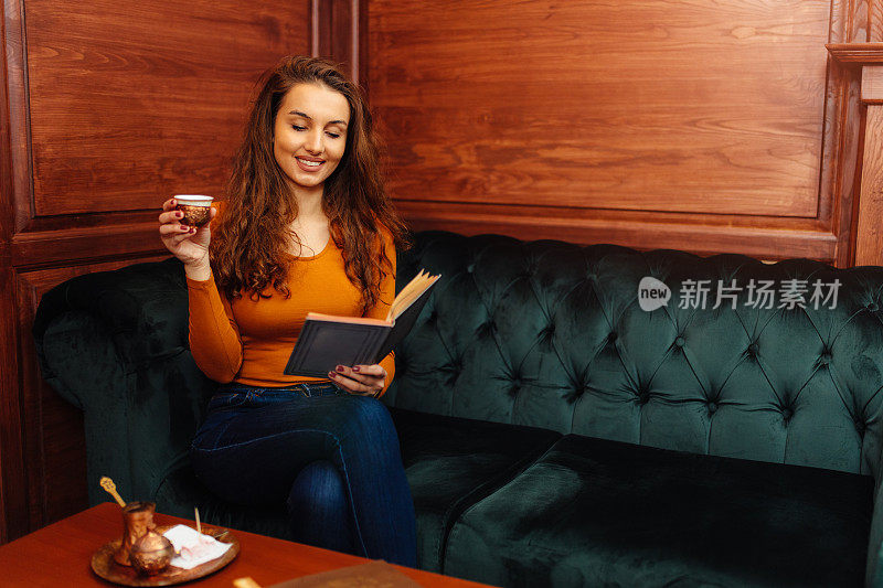 美丽的年轻女子一边喝咖啡一边看书