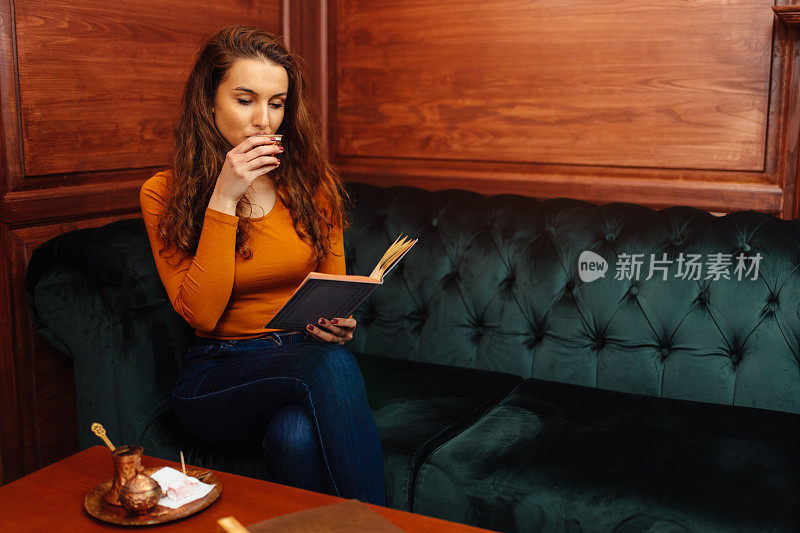 美丽的年轻女子一边喝咖啡一边看书