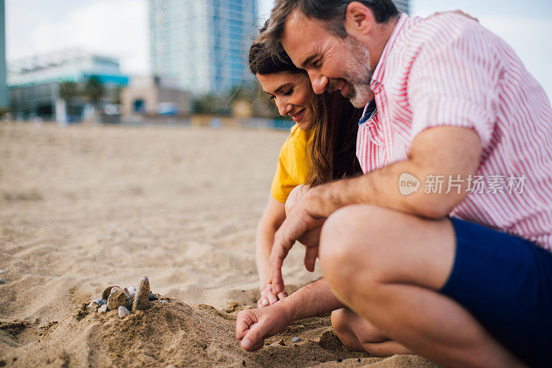 一对情侣在海滩上建城堡，面带微笑