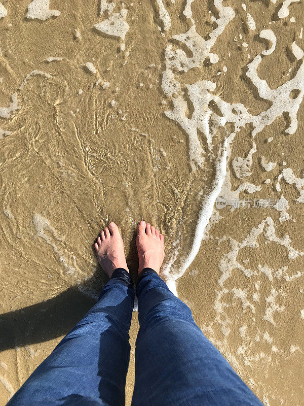 英国伯恩茅斯海滩，阳光明媚的一天，白色的英国人的脚在金色的沙滩上被海浪拍打着海岸线，赤脚用脚趾走路，海边的脚印站在海滩上