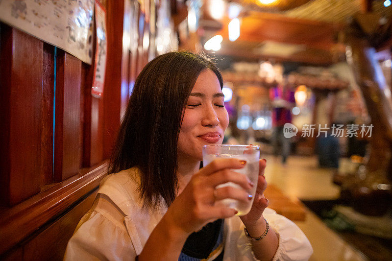 一名年轻女子对居酒屋餐厅的日本“Awamori”酒很满意