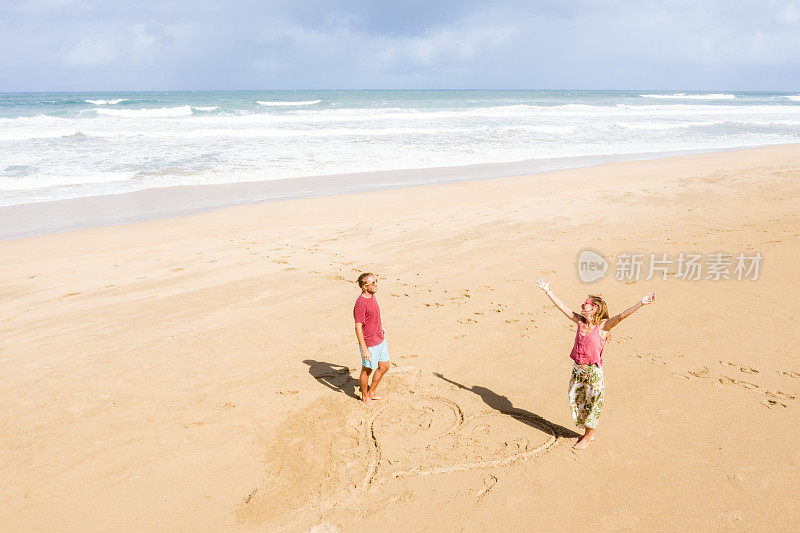 无人机上的年轻夫妇站在海滩上靠近画的心在沙滩上