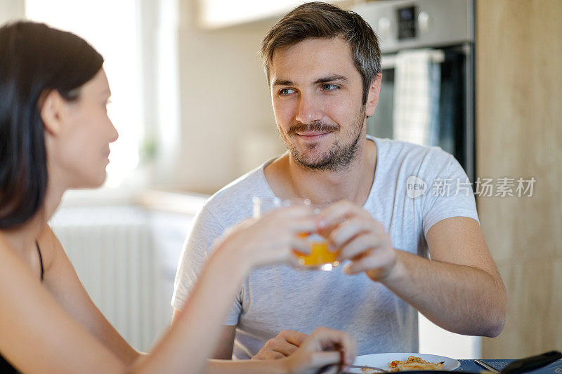 一对年轻夫妇在吃早餐时喝着橙汁