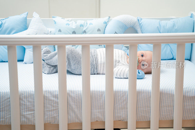 可爱的婴儿躺在他的婴儿床上，用奶嘴吮吸着镜头
