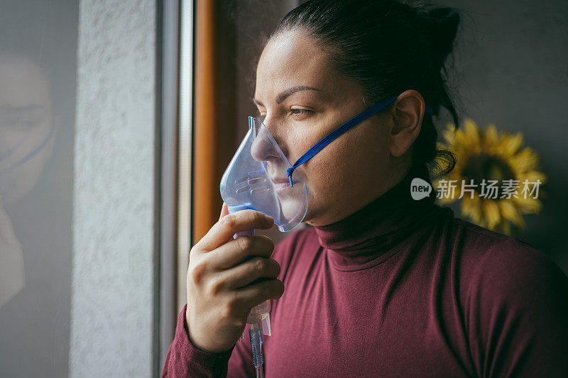 一名年轻女子在自我隔离期间吸着烟，望着窗外。