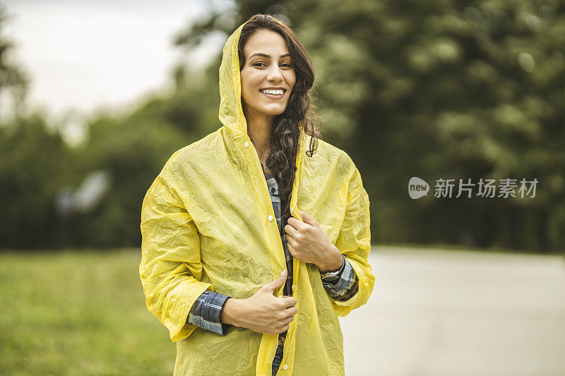 快乐的年轻女子穿着黄色雨衣，享受着雨