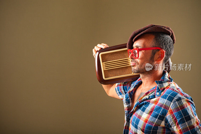 一个戴着红眼镜微笑着的男人，正在听老式收音机