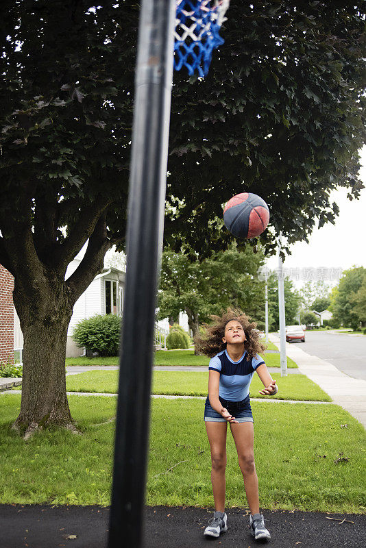 混血少女在郊区的车道上练习篮球。
