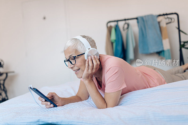 成熟的女人戴着耳机享受在她的床上和打视频电话