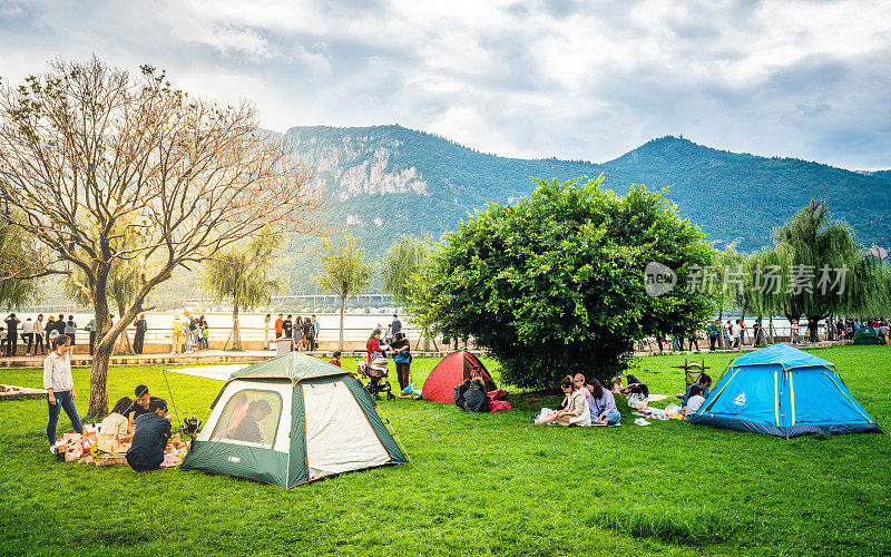 在中国云南昆明的滇池海埂公园里，人们在草地上、湖上和西山上搭帐篷享受假期