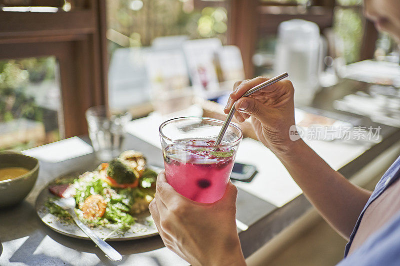 在一家素食咖啡馆里，一位女士正在用一根可重复使用的不锈钢吸管喝红色紫苏汁。