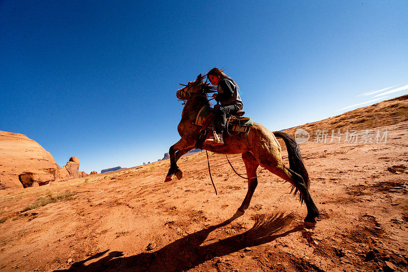 一个年轻的纳瓦霍男孩骑着一匹小马在亚利桑那纪念碑谷的骆驼丘附近的沙漠平原上跳跃，纪念碑谷部落公园