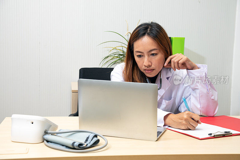 亚洲成年女医生在笔记本电脑上查看病人记录，并在房间里做记录总结