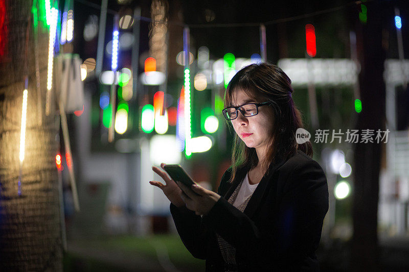 亚洲中国女人看着智能手机与担忧的表情脸在夜晚的街道上。