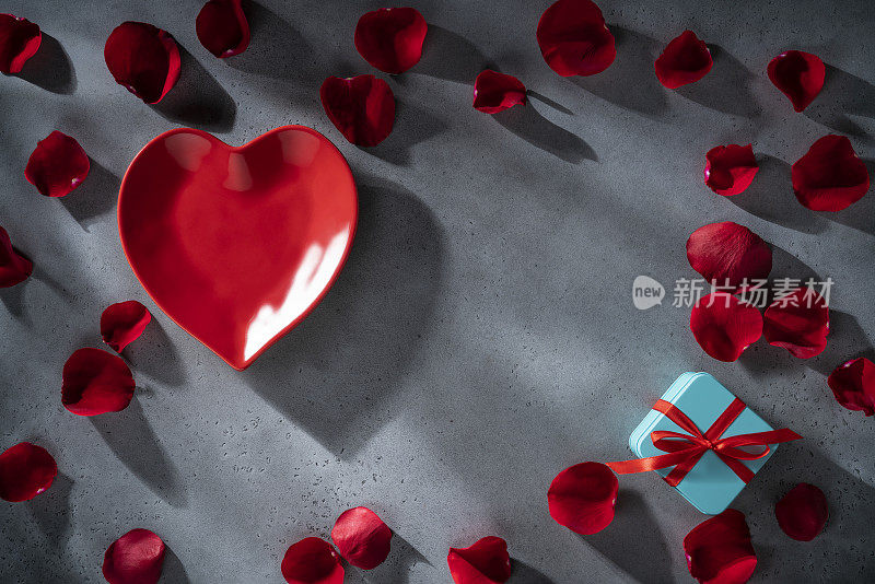 情人节红玫瑰花瓣和红色的心型板在灰色的背景