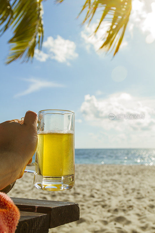 美国，迈阿密，南佛罗里达，迈阿密，比斯坎岛，迈阿密海滩，一个年轻人拿着一杯冰冻啤酒站在天堂般的风景蓝色大海前