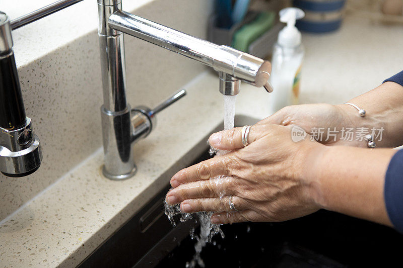 一个女人的手正在厨房水槽的自来水下清洗的特写