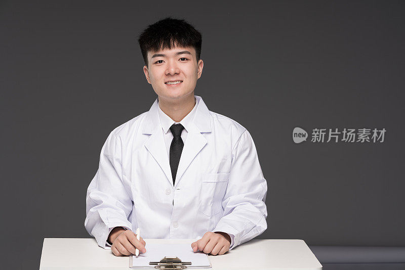一位年轻的亚洲男医生坐在他的办公桌前