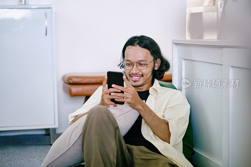 年轻的亚洲男人在家里玩智能手机